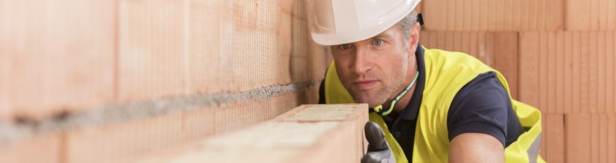 Construction worker checking alignment of mineral-wool filled clay block