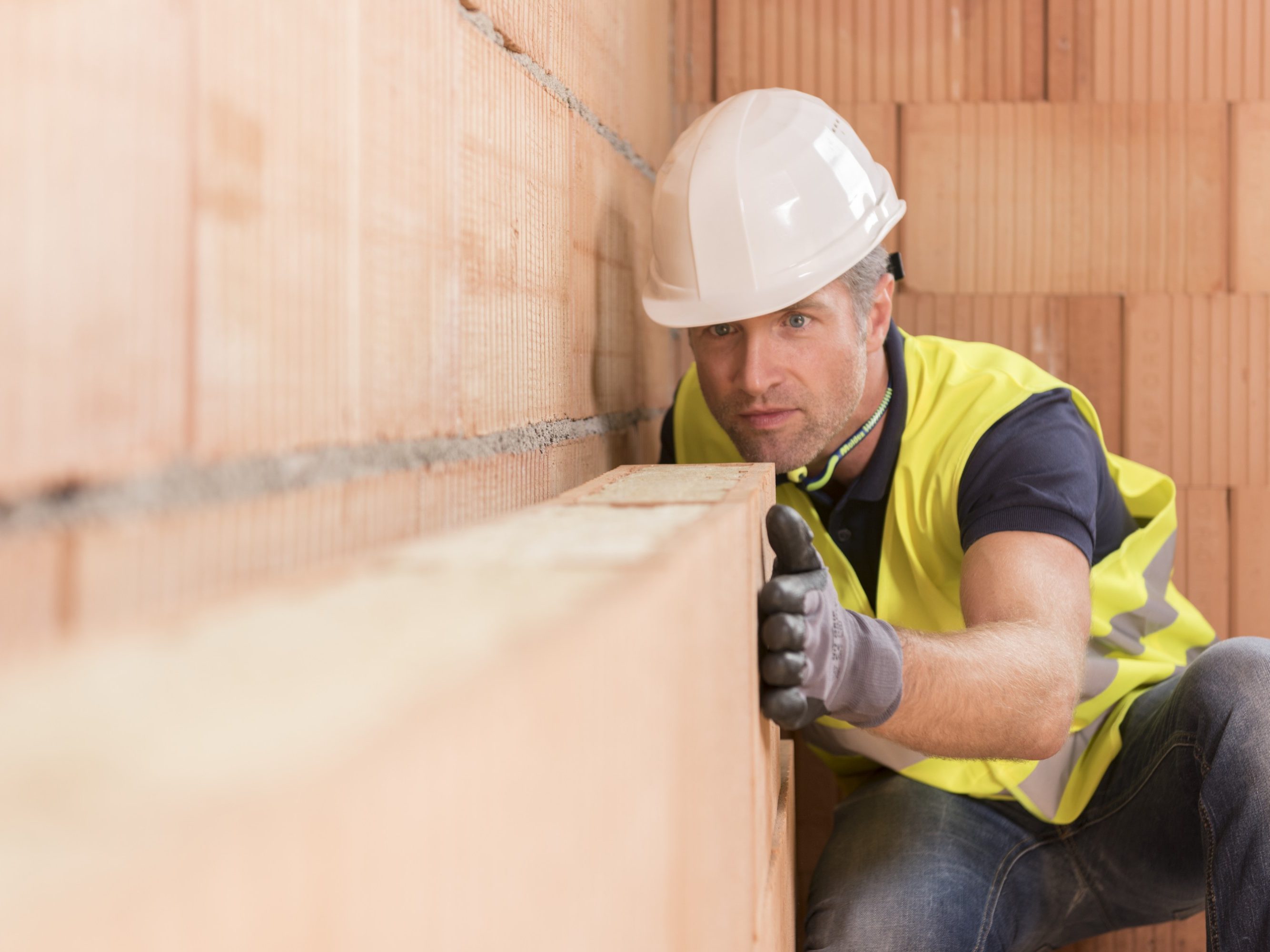 Construction worker checking alignment of mineral-wool filled clay block