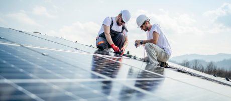 Team of two workers on a house's roof installing solar panels.
