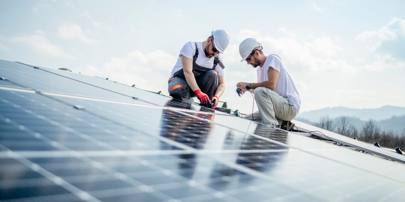 Team of two workers on a house's roof installing solar panels.