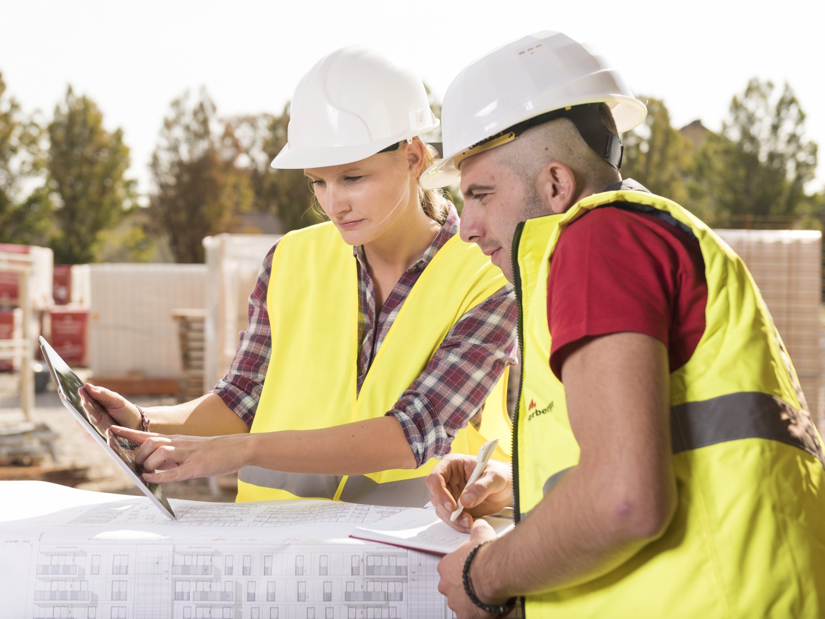 Woman pointing at tablet with male coworker taking notes at construction site, Fast Forward Commercial Excellence