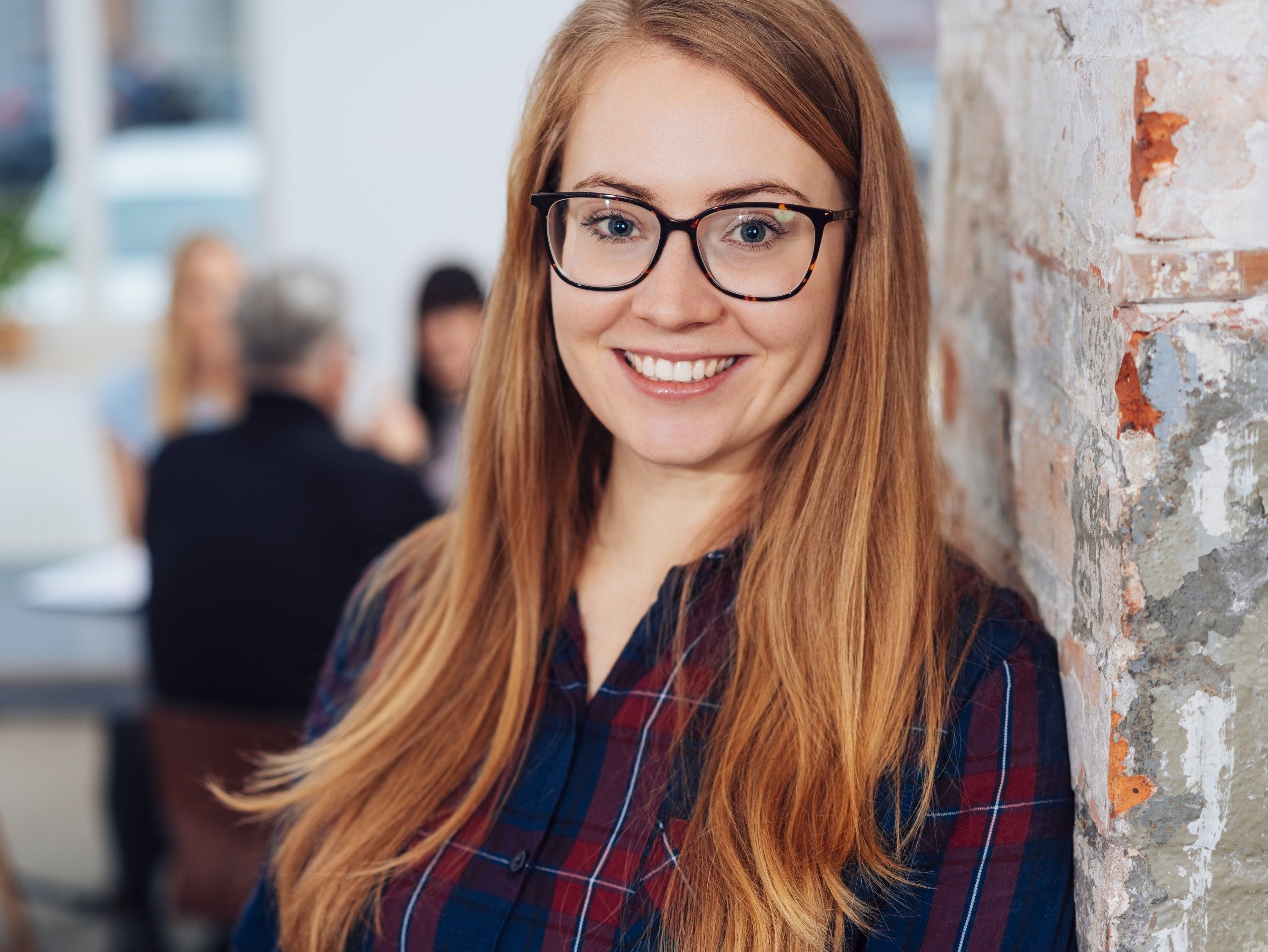 Smiling young businesswoman wearing glasses in a close up cropped portrait in an office with colleagues in the background