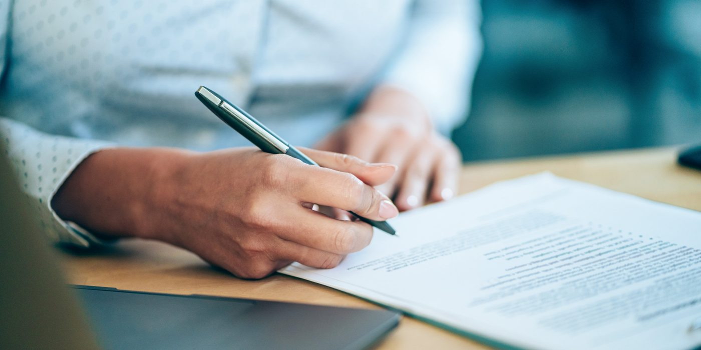 Close-up shot of a businesswoman holding a pen and signing contract.