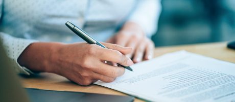 Close-up shot of a businesswoman holding a pen and signing contract.